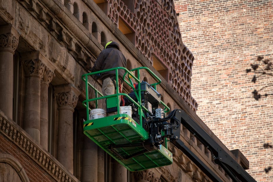A Hitachi compact excavator performing masonry work, lifting a pallet of bricks to a scaffold platform - construction equipment rentals Madison WI