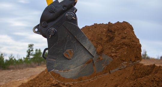 An excavator bucket on a quick coupler scooping dirt