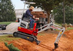 A Takeuchi mini excavator with its operator standing beside it