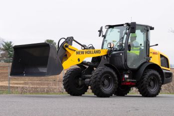 A New Holland compact wheel loader with an empty bucket on pavement