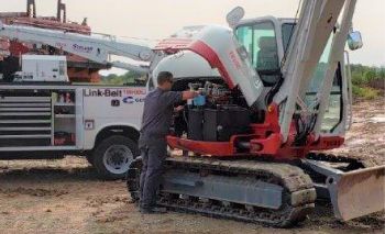 A technician at a Link-Belt service truck working on a Takeuchi excavator in the field