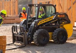 A New Holland skid steer carrying pallet forks on a job site