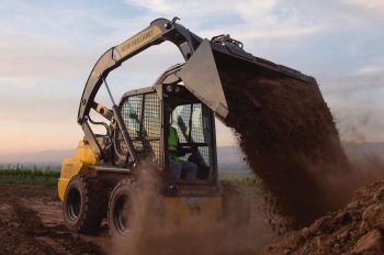 A New Holland skid steer dumping a bucket of dirt