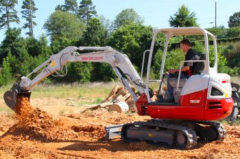 A Takeuchi TB230 compact excavator digging in red clay
