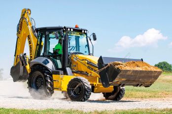 A New Holland tractor loader backhoe carrying a full loader bucket on a gravel road